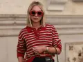 Donna con occhiali rossi oversize e maglione a righe rosse e bianche, un look che evoca un sofisticato preppy style.