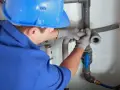 Instalator w niebieskim kasku i rękawicach montuje elementy instalacji kanalizacyjnej.