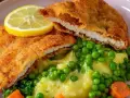 Pyszne schabowe z piekarnika, podane z puree ziemniaczanym, groszkiem i marchewką. Całość ozdobiona plasterkiem cytryny.