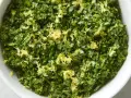 Un cuenco blanco lleno de perejil picado y ralladura de limón, perfecto para un toque fresco en tu cocina, como la albahaca en francés.