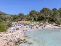 Słoneczna plaża z turkusową wodą, parasolami i ludźmi wypoczywającymi na piasku. To jedno z najpiękniejszych miejsc na Majorce.