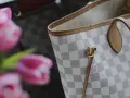 Jasna torebka Louis Vuitton w kratkę Damier Azur z różowymi tulipanami w tle.