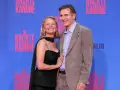 Liam Neeson e Pamela Anderson sorridono sul tappeto blu, con lo sfondo di "Die Nackte Kanone".