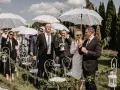 Wesele w kwietniu pod białymi parasolami. Goście w eleganckich strojach, wśród nich pan młody z bukiecikiem.