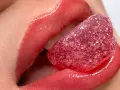 Labbra carnose e lucide, con un effetto volume dato da un tatuaggio labbra, assaporano una caramella rossa zuccherina.