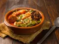 Un humeante pote asturiano, con fabes, berzas, chorizo y tocino, servido en cazuela de barro sobre arpillera.