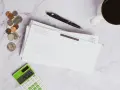 Stos monet, koperta, długopis, kalkulator z kwotą 1425,65 i kawa. Może to być rachunek z odsetkami komorniczymi.