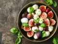 Un tazón lleno de bolitas de mozzarella fresca, higos cortados y hojas de albahaca, perfecto para ensaladas saludables.