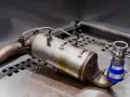 Element układu wydechowego diesla, potencjalnie z objawami zapchanego EGR. Widoczny metalowy cylinder z rurkami i zaciskami.
