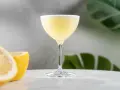 En elegant lemon martini med en lätt skumkrona, serverad med färska citronklyftor i bakgrunden.