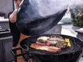 Fumo sale da una grigliata di carne succulenta, con salsicce, hamburger e pancetta che sfrigolano.