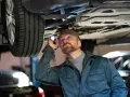 Mechanik z latarką bada podwozie auta, szukając problemów z jarzmem hamulca.