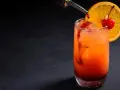 Kolorowy drink z syropem grenadina, ozdobiony plasterkiem pomarańczy i wisienką.