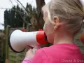Ein Mädchen mit blonden Zöpfen hält ein Megafon und schreit hinein. Vielleicht fragt sie sich, warum sind Kinder so laut?