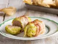Deliziosi involtini di verza con carne, avvolti in pancetta croccante, serviti su un piatto bianco con bordo verde.