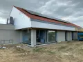 Budowa domu z dachówką i panelami słonecznymi. Dach bezokapowy z widoczną izolacją styropianową i oknami.