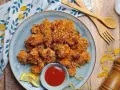 Piatto di croccanti bocconcini di pollo impanati con fiocchi di mais, serviti con ketchup e spicchi di limone.