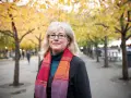 Kvinna med glasögon och färgglad scarf i höstpark. Hon verkar inte ha ont i leder brist på energi, utan njuter av den vackra naturen.