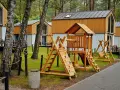 Drewniany plac zabaw z domkami w tle. Idealne bory tucholskie atrakcje dla dzieci, gdzie można odpocząć i pobawić się na huśtawkach i zjeżdżalni.