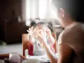 Niania karmi dziecko, które trzyma zabawkę. Zastanawiasz się, ile kosztuje godzina niani do dziecka?