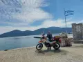 Kobieta z motocyklem nad morzem, z grecką flagą powiewającą na wietrze. Piękny dzień na podróż motocyklem nad morze.