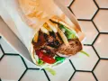 Kebab zawinięty w papier, z mięsem, frytkami, sałatą i pomidorem.