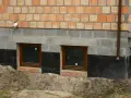 Fundamenty starego domu wymagają wzmocnienia. Widoczne okna piwniczne, izolacja i nowe mury świadczą o pracach.
