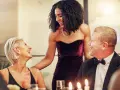 Drei Personen in eleganter Galadinner Kleidung lachen und unterhalten sich bei Kerzenlicht.