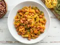 Pasta all'uovo con fagioli borlotti in una ciotola bianca, con fagioli secchi e pasta fresca colorata sullo sfondo.