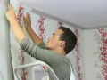 Mann tapeziert mit roter Blumenmuster-Tapete die Decke.