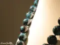 Collana di sfere in crisocolla pietra, con sfumature blu e nere, su sfondo chiaro e scuro.