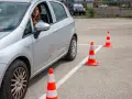 Młoda kobieta za kierownicą srebrnego samochodu ćwiczy jazdę na placu manewrowym. To może być jej droga do zdobycia prawa jazdy 17 lat.