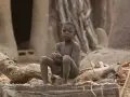 Chłopiec siedzi na pniu drzewa w wiosce w Togo, Afryka.