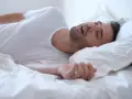 Mężczyzna śpi na boku, z otwartymi ustami i widocznym chrapaniem.