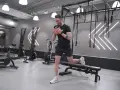 Man utför rumplyft på gym med kettlebell. Träningsredskap som roddmaskiner och ringar syns i bakgrunden.