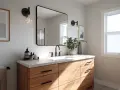Une salle de bain moderne avec un meuble-lavabo en bois clair, un grand miroir, des luminaires industriels et une plante verte. Idéal pour peindre une salle de bain.