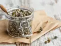 Barattolo di vetro pieno di capperi sotto sale, con alcuni sparsi sul foglio di carta marrone.