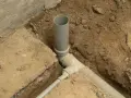 Fragment budowy kanalizacji. Szare rury układane są w wykopie, otoczone ziemią i fragmentami betonu.