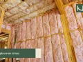 Wnętrze domu w trakcie budowy, ściany i sufit wypełnione różową wełną mineralną. To kluczowy etap, jak wyciszyć pokój, zapewniając komfort akustyczny.