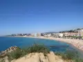 Vista panorámica de la playa S'Abanell en Blanes, con el mar azul intenso, arena dorada repleta de gente y edificios costeros bajo un cielo despejado.