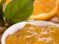 Una ciotola di marmellata di arance, con fette di arancia e foglie verdi sullo sfondo. Un'idea per un delizioso pesto al limone.