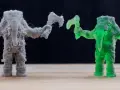A grey FDM printed elephant warrior with stringing, and a translucent green resin printed elephant warrior, showcasing the difference between FDM vs resin printing.