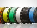 Kolorowe szpulki z materiałami do drukarki 3d: czerwony, pomarańczowy, żółty, zielony, biały, czarny, niebieski i kremowy.
