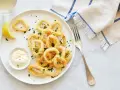 Crujientes calamares a la romana, servidos con limón y salsa tártara en un plato blanco.