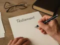 Dłoń pisze piórem na dokumencie z napisem "Testament". Obok leżą okulary i oprawiona księga.