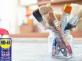Un bote de WD-40 y un frasco de vidrio con varios pinceles sucios, listos para limpiar.
