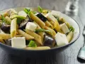 Piatto di pasta con melanzane in bianco, cubetti di formaggio fresco e foglie verdi.