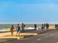 Ludzie spacerują i jeżdżą na rowerach wzdłuż promenady nad oceanem w słoneczny dzień.