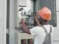 Elektryk w kasku sprawdza instalację fotowoltaiczną. Dowiedz się, jak obniżyć napięcie w sieci fotowoltaika.