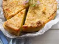 Delizioso gateau di patate dorato e croccante, guarnito con rosmarino fresco. Una fetta è già stata tagliata, invitando ad assaggiarlo.